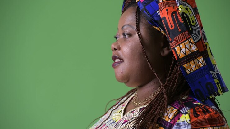 Overweight beautiful African woman wearing traditional clothing against green background