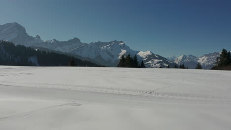 Drohne-Fliegt-Tief-über-Schneebedecktes-Feld,-Steigt-Langsam-Auf-Und-Enthüllt-Ein-Wunderschönes-Grünes-Tal