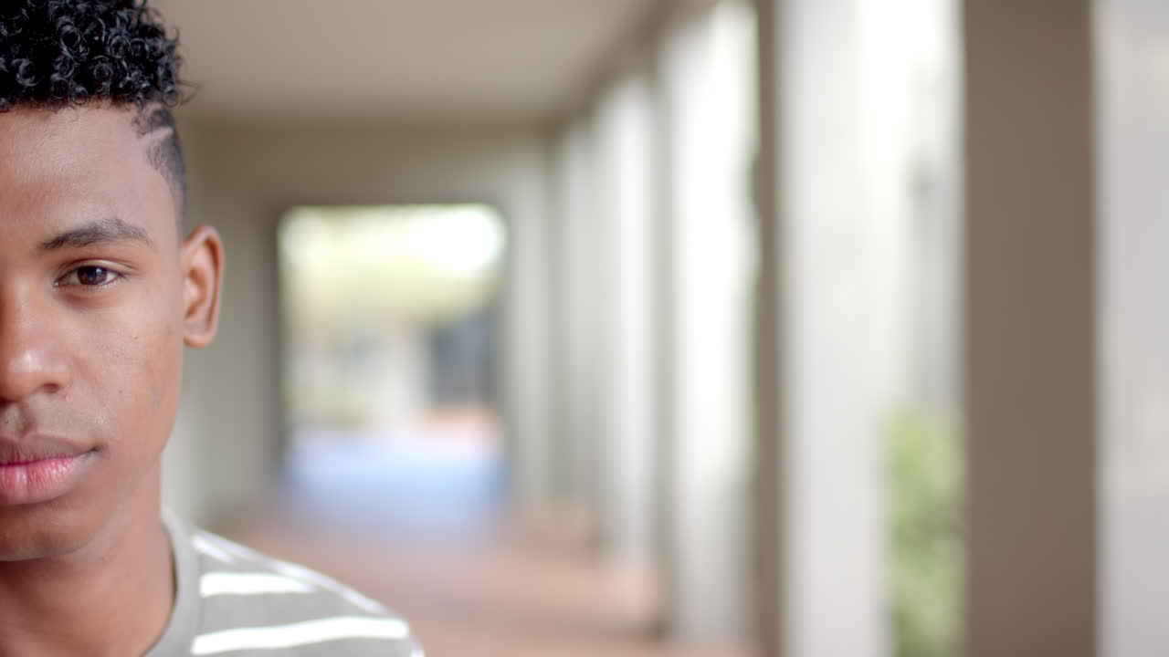 Teenage biracial boy stands in a high school corridor, with copy space