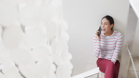 Happy-biracial-woman-sitting-on-stairs-talking-on-smartphone,-copy-space,-slow-motion