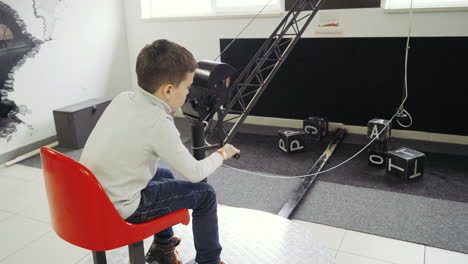 boy sits in the excavator simulator and plays with the joystick. transportation of steel cubes using a magnet.