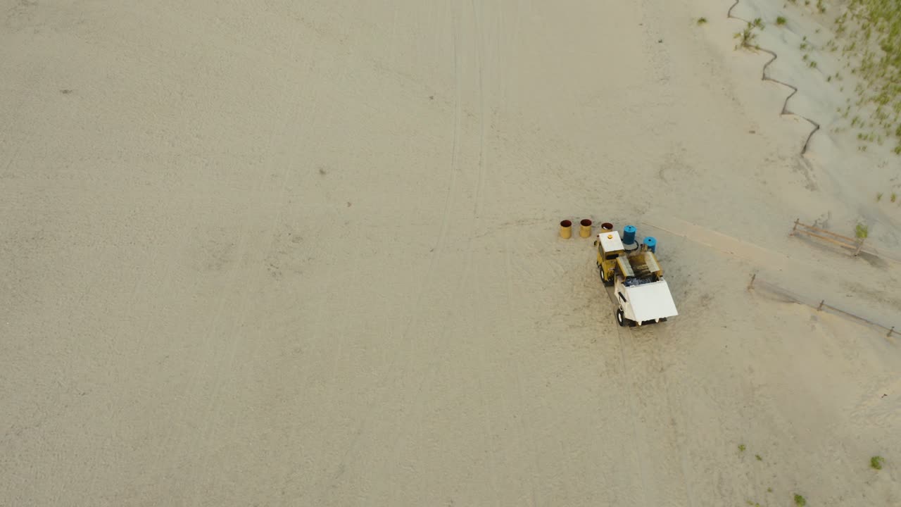 Aerial, buggy with robotic arm emptying trash bins on public beach