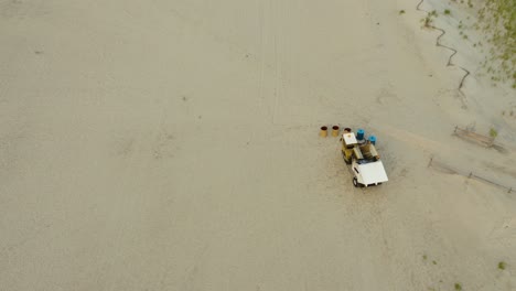 aerial, buggy with robotic arm emptying trash bins on public beach