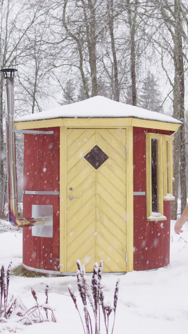 Uomo trasandato cammina in asciugamano e stivali nella neve ed entra in una sauna di legno, verticale.