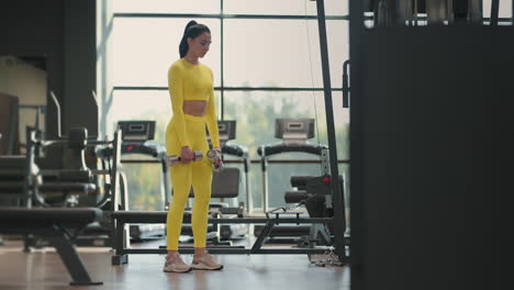 fit hispanic woman performing weight lifting deadlift exercise with dumbbell at gym in yellow sportswear. woman brunette fitness performing doing deadlift exercise with dumbbell