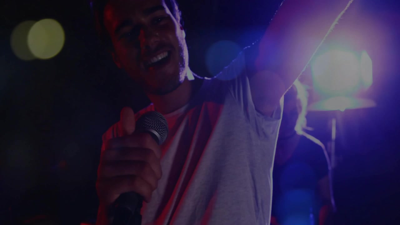 Male music performer adjusting mic, leaning into mic and singing, engaging crowd amid blue lights