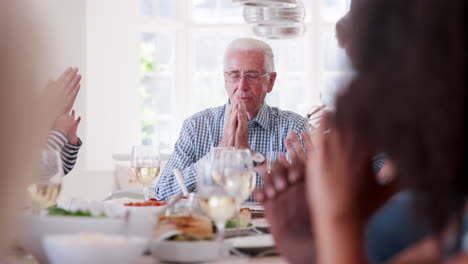 slow motion shot of multi-generation family and friends around table praying before meal at party