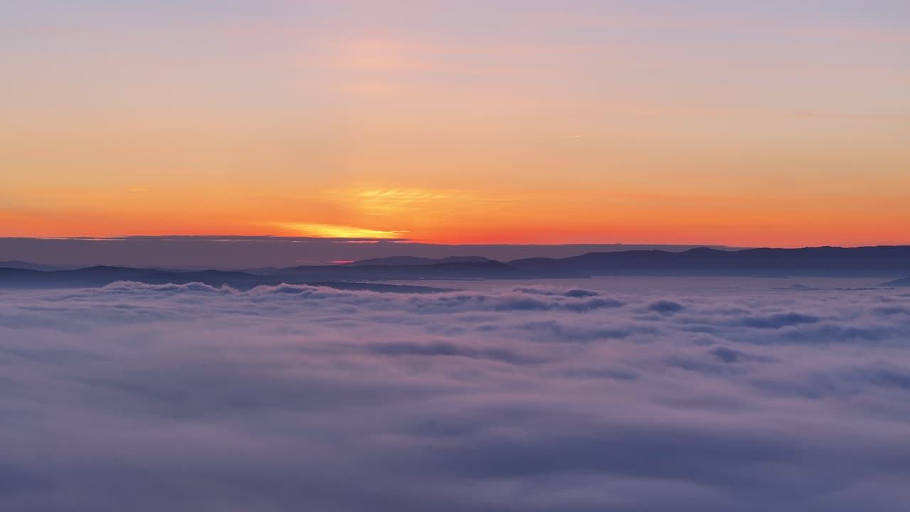 Coucher de soleil à couper le souffle depuis une montagne, nuages et brume recouvrant les basses terres.