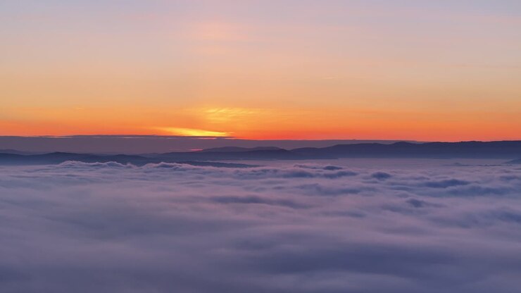 Tramonto mozzafiato da una montagna con nuvole e nebbia che coprono la terra sottostante