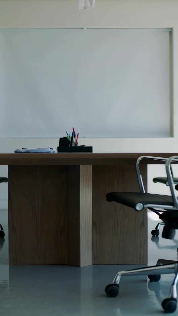 Video vertical: Silla giratoria rotando y moviéndose a la derecha sobre una mesa de reuniones, mostrando un portalápices y papeles.
