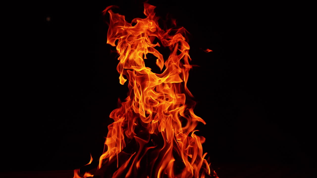Big campfire burning at night. Isolated bonfire at black backdrop. Long flame stretching up high.
