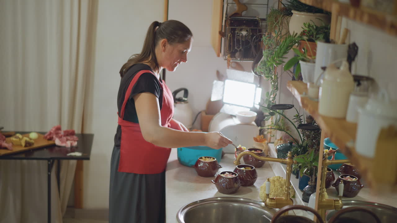 Mulher branca na cozinha de casa preparando o jantar com tigela azul e utensílios, bancada movimentada com pratos e plantas, misturando ingredientes sobre a pia, preparação de refeição organizada para a família, luz natural quente, espontâneo