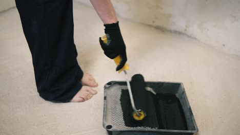 the girl painting wall with roller in the room with a black paint she stands opposite that wall. slow motion