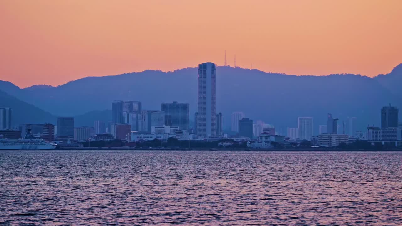 Una ripresa in timelapse dello skyline urbano di George Town durante il tramonto, con l'imponente Torre Komtar e navi da crociera che solcano il mare