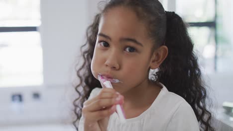 retrato de una feliz chica biracial mirando a la cámara y cepillándose los dientes