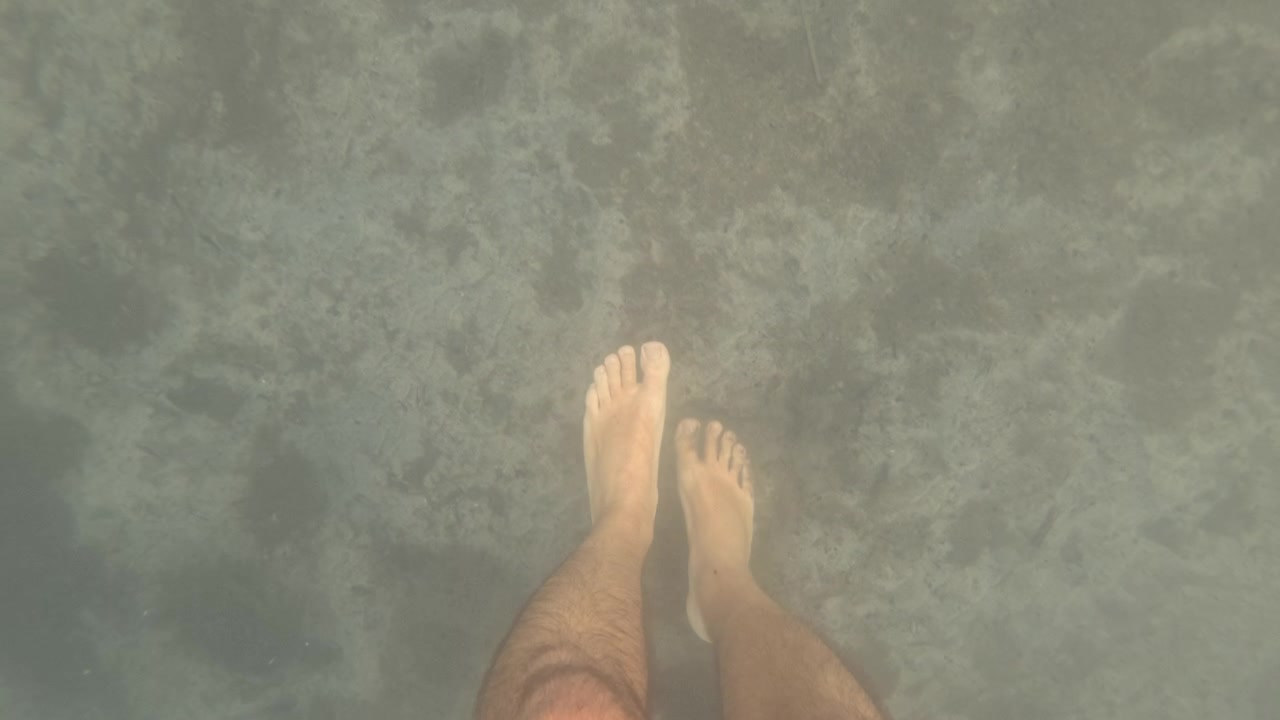 Underwater view of a swimmer's foot walking over a murky, sandy seafloor, Golfe-Juan, France