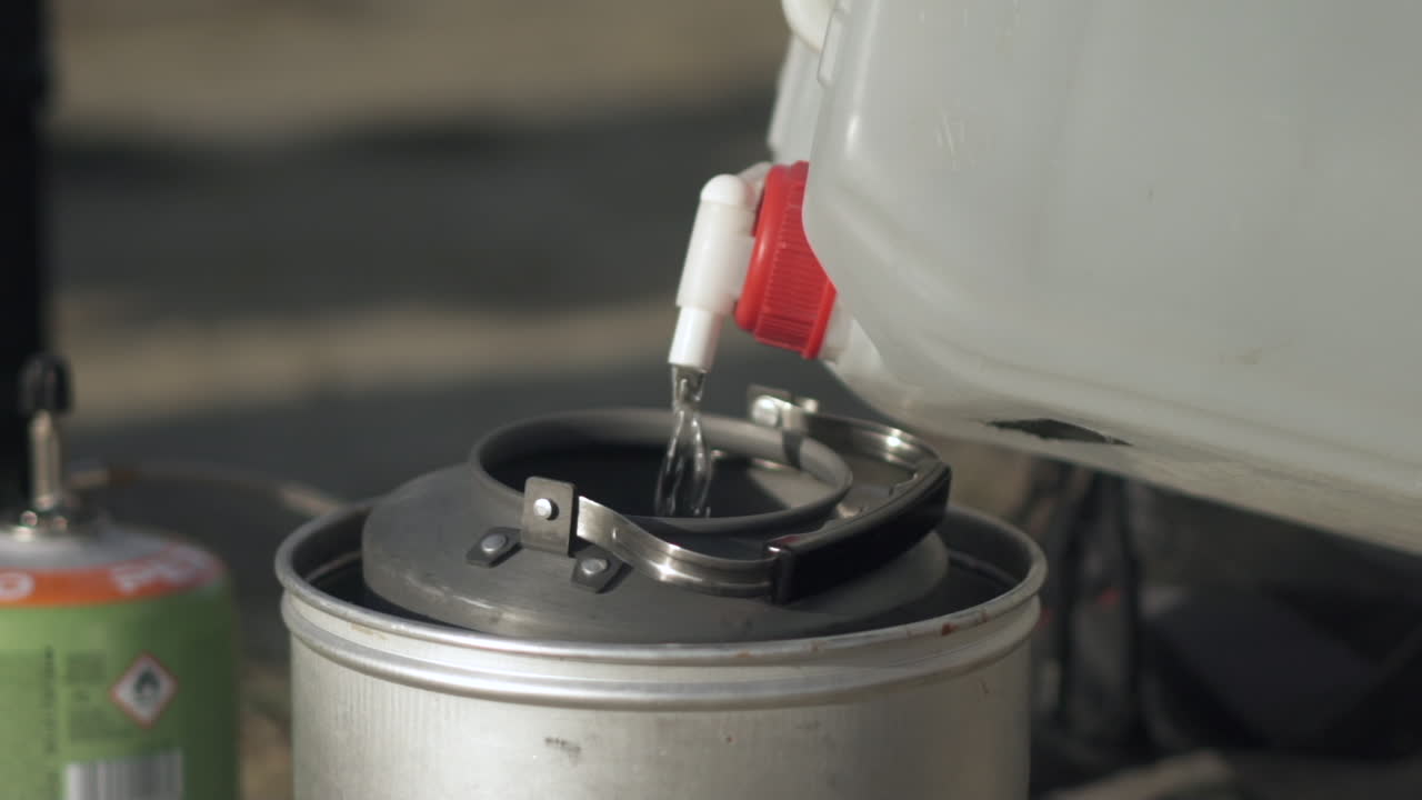 물이 플라스틱 용기에서 금속 캠핑 플라스크로 슬로우 모션으로 쏟아집니다