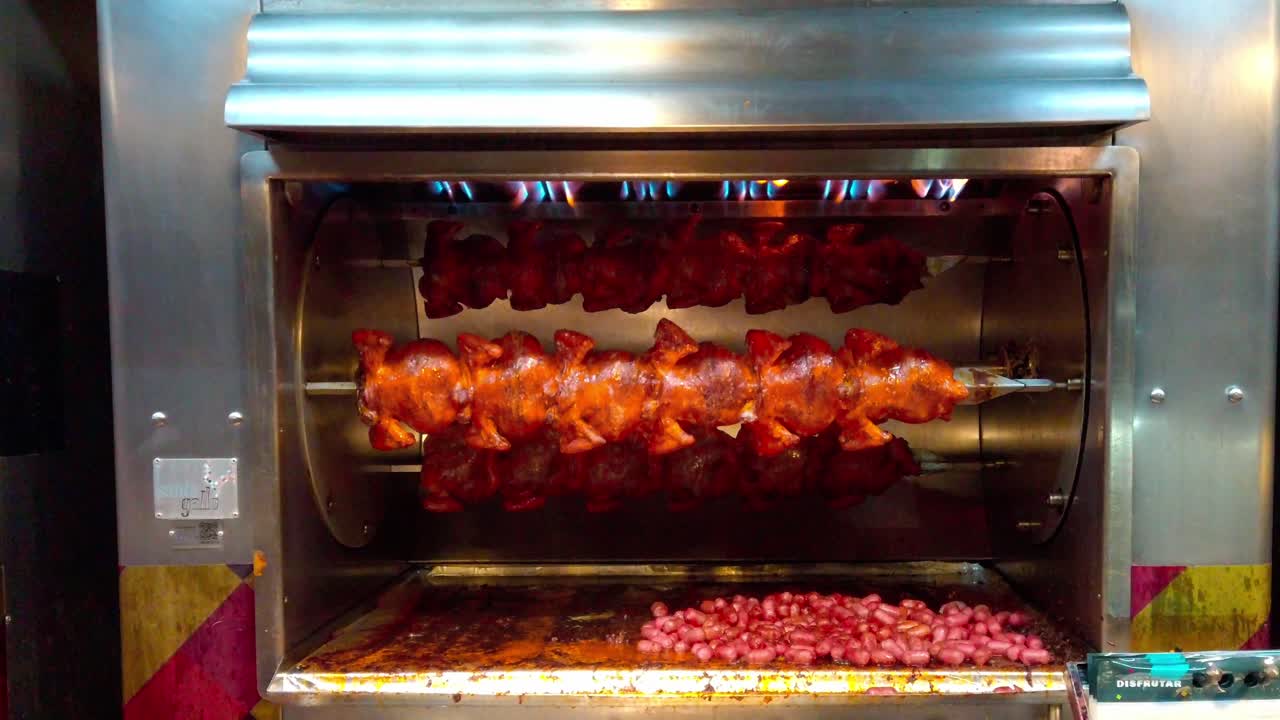 Roasting meat on a spit with vegetables cooking below, close-up shot of rotisserie in action