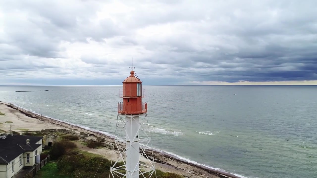 Un drone orbita il Faro di Pape mentre nuvole di pioggia scure si addensano sopra la costa del Mar Baltico.