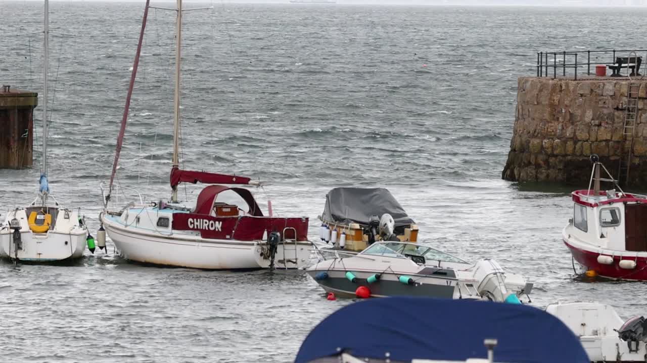 Una varietà di piccole imbarcazioni e yacht galleggiano su acque agitate vicino a un molo di pietra.