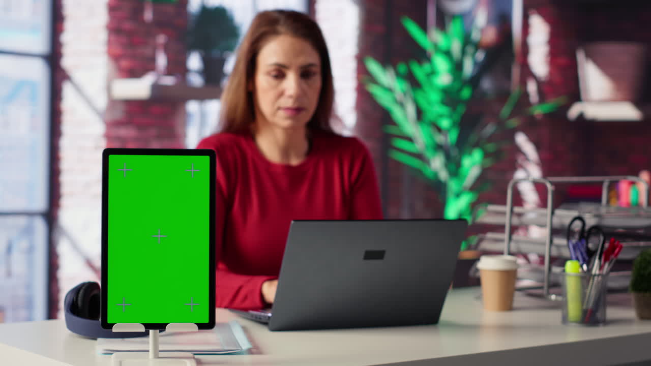 Woman working with laptop and tablet with green screen