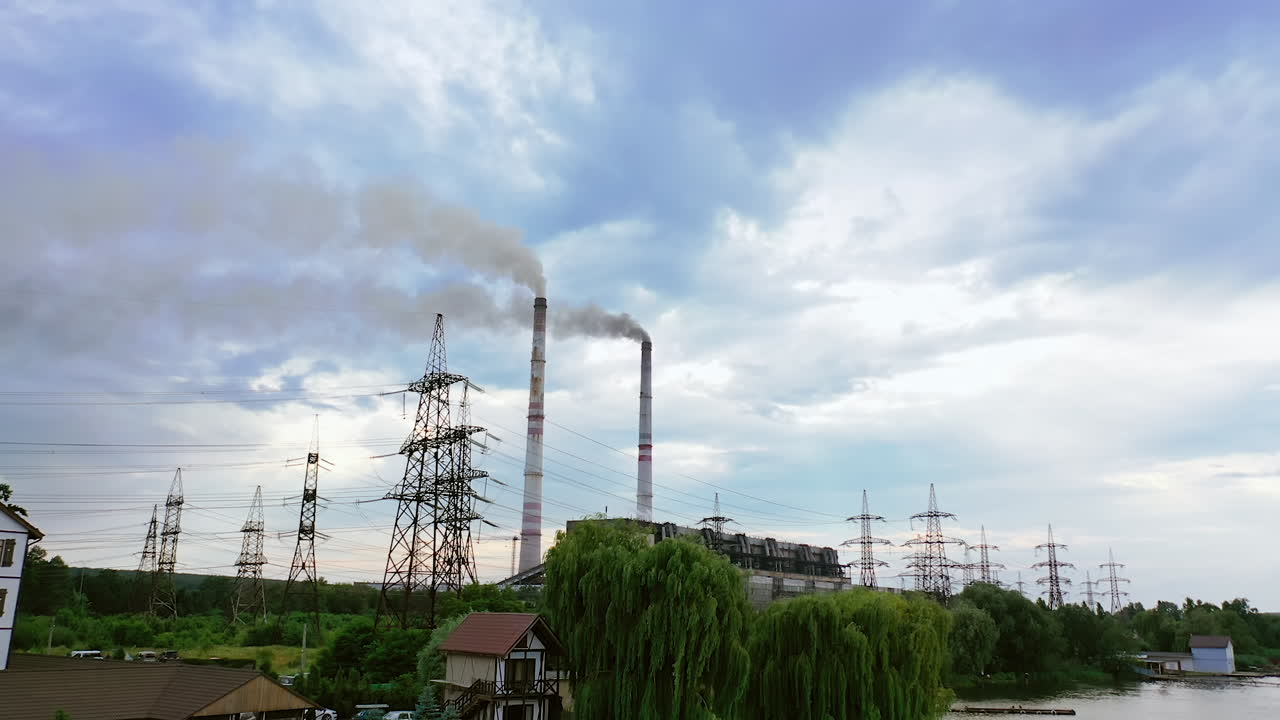 Manufacturing with chimneys among nature. Harmful industrial territory with smoke going from factory. High-voltage electric towers in the countryside. Air pollution.