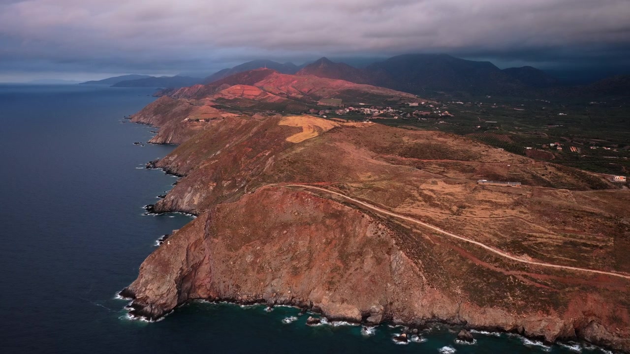Vista aerea con drone di un promontorio spoglio e di una costa frastagliata sotto montagne luminose, Panormos, Grecia