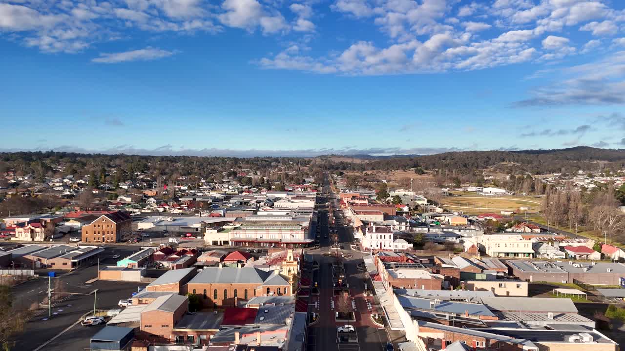 Drone camera glides above Glen Innes’ central street, revealing urban buildings, light traffic, and clear blue skies in bright daylight