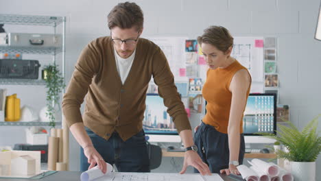 arquitectos masculinos y femeninos en la oficina desenrollando el plan o el plano y colocándolo en el escritorio