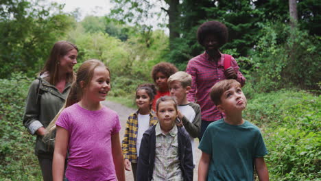 adult team leaders with group of children at outdoor activity camp walking through woodland