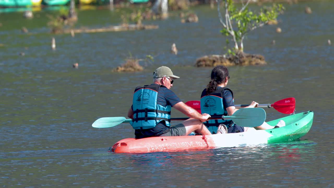 A couple in life vests paddles a tandem kayak through calm mangrove waters in Thailand