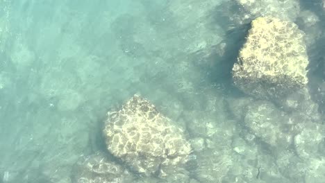 Clear-water-on-a-sunny-day,-reflecting-the-light-and-revealing-the-bottom-with-some-rocks-in-Portugal