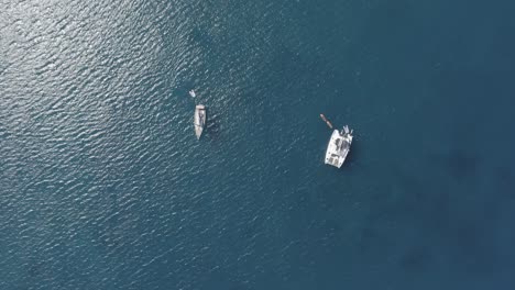 an aerial birds eye view of two sailboats in the sea with the sun at midday