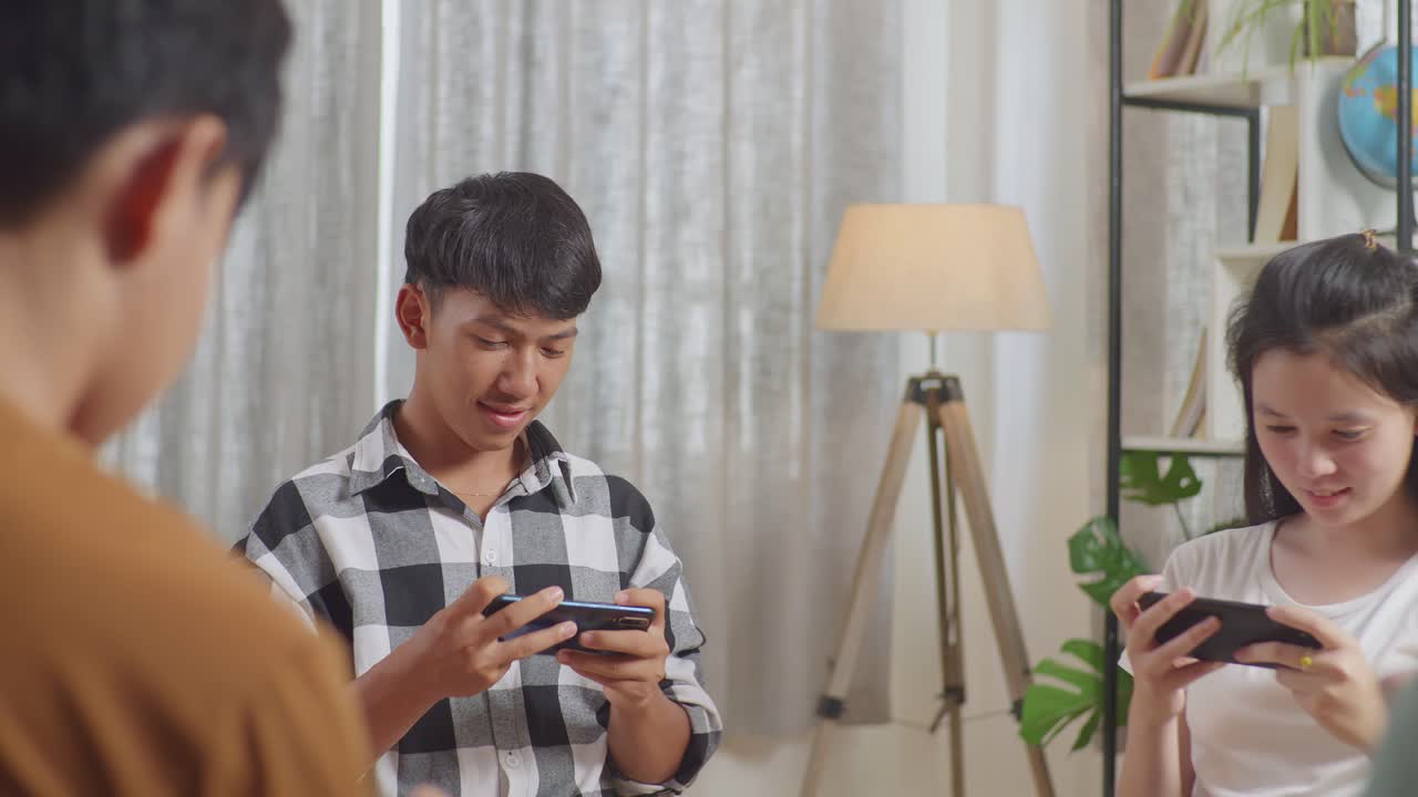 집에서 스마트폰으로 게임을 하는 원을 형성하는 의자에 앉아있는 아시아 십대 그룹의 클로즈업