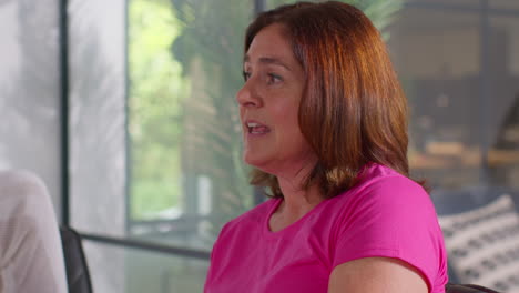 mujer madura sonriendo y riendo hablando en una reunión del grupo de apoyo de terapia para pacientes de tratamiento de cáncer de mama sentada en la mesa