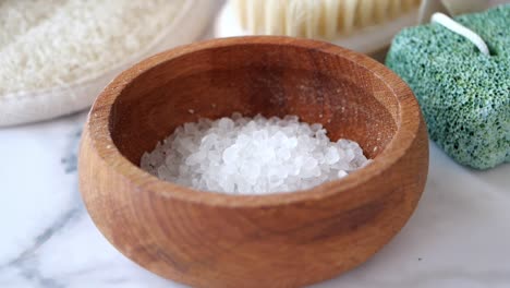 close-up of a wooden bowl filled with white bath salts, next to a green stone and a white brush