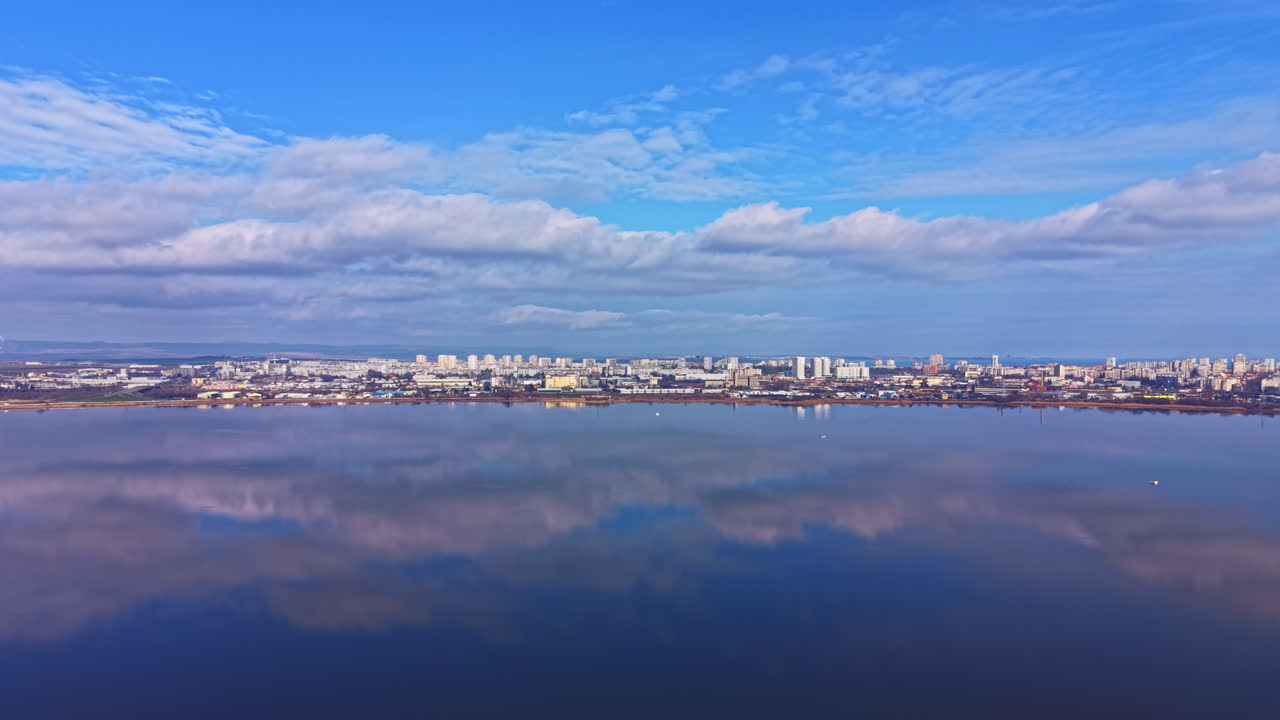 澄み渡る空の下、昼間の穏やかな水面に、雲を背景にした都市のスカイラインが映る。