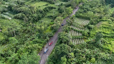 aerial view of sand trucks passing through green plains, slope of merapi volcano, indonesia.