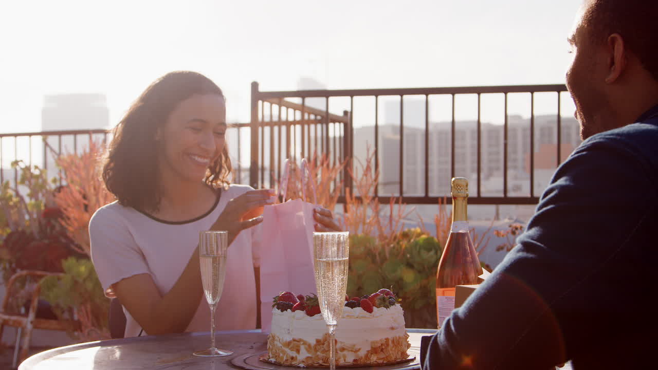 hombre dando regalo y tarjeta a la mujer mientras celebran en la terraza de la azotea con el horizonte de la ciudad en el fondo