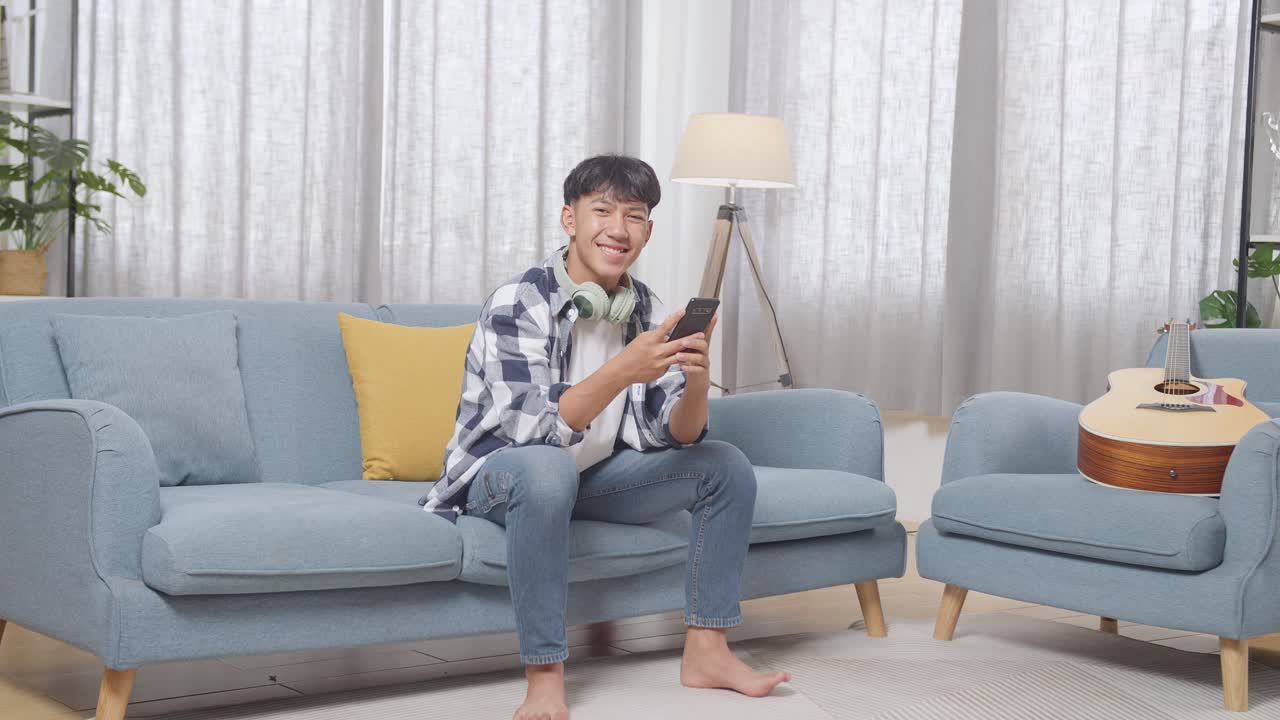 십대가 스마트폰을 사용하여 소파에서 휴식을 취하고 있습니다.