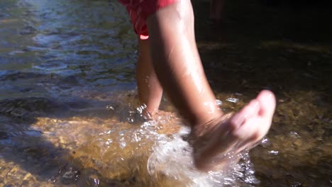 Slow-motion-shot-of-a-young-child's-feet-kicking-water-in-a-stream