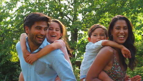 Portrait-Of-Family-Outdoors-In-Garden-Or-Countryside-With-Parents-Giving-Children-Piggybacks