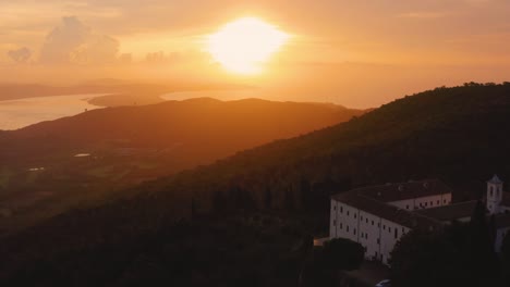 aerial drone footage of the sunrise at the iconic monte argentario lagoon, facing the old town orbetello and a monastery close to maremma nature park in tuscany, italy, with dramatic clouds