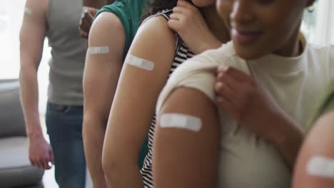 Mid-section-of-group-of-diverse-young-people-showing-their-vaccinated-shoulders-at-home