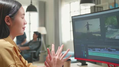 asian female video editor stretching while works with footage and sound on her personal computer in office