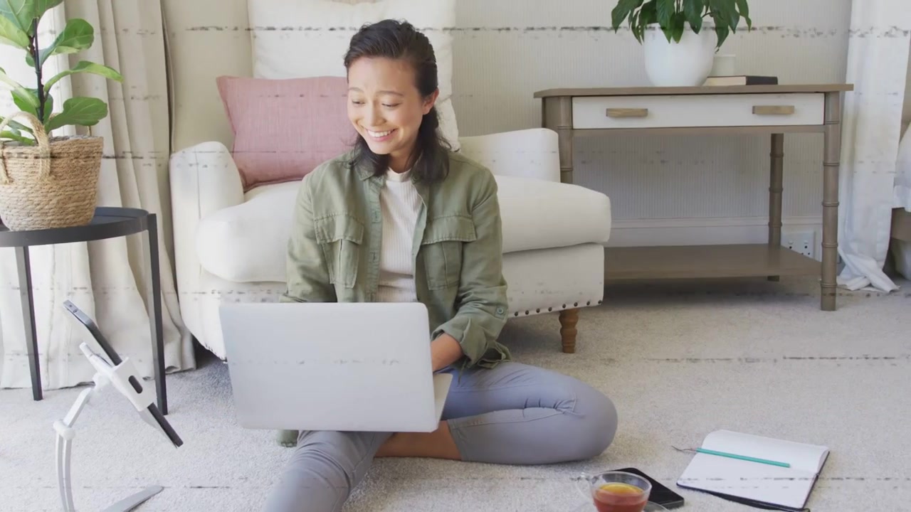 グリッチエフェクトが晴れていく中、ノートパソコンで作業し、タイピングしながらリモートワークのためにノートを確認する女性。
