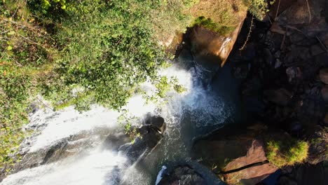 drone aerial shot from forest and approaching a tropical waterfall in brazil from above in daylight and showing the water with a colorful rainbow