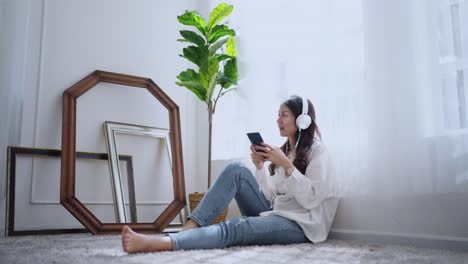 attractive casual asian female adult woman listen music headphone positive emotion sit on floor next to window pleasure and peaceful smiling relax,asia woman using smartphone at home daytime casual