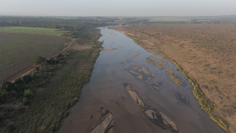 Push-forward-drone-view-of-seasonal-or-ephemeral-crocodile-river-by-sugarcane-farmlands-bordering-the-Kruger-National-Park