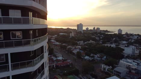 Aerial-drone-footage-of-high-rise-apartment-building-with-a-view-of-the-city-at-sunset